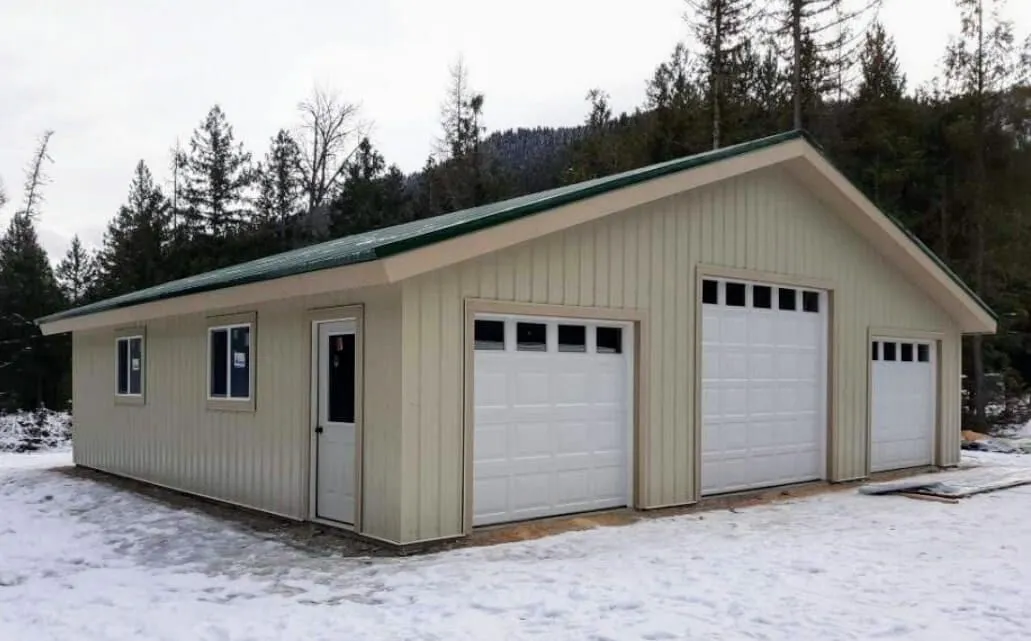 A garage with three garage doors and a green roof in the snow.