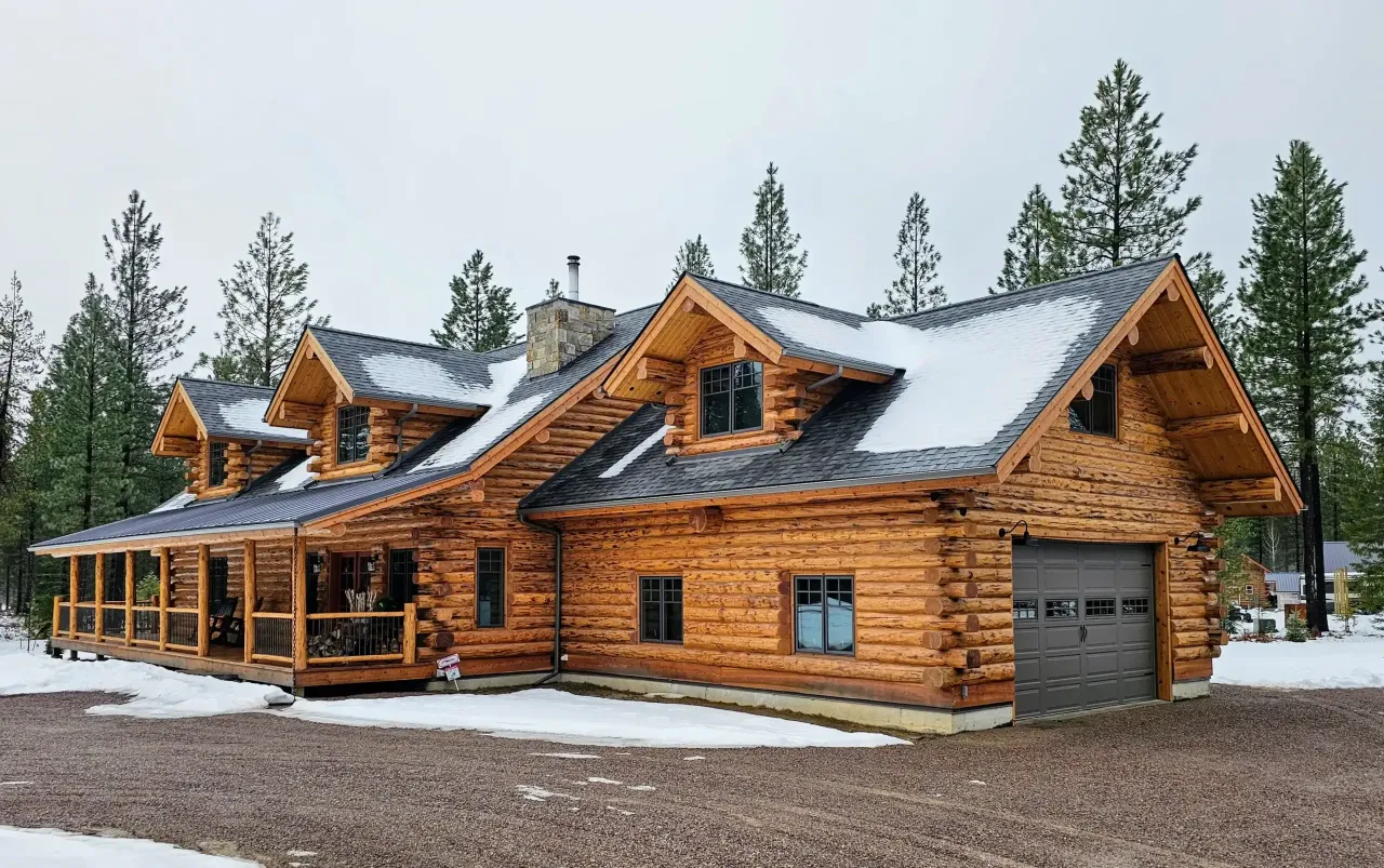 A large log cabin with a garage and porch in the snow.