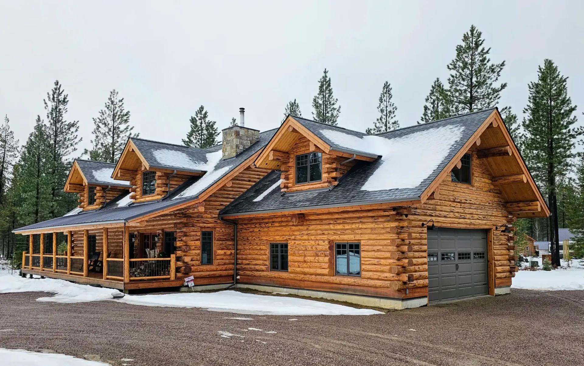 A large log cabin with a garage and porch in the snow.