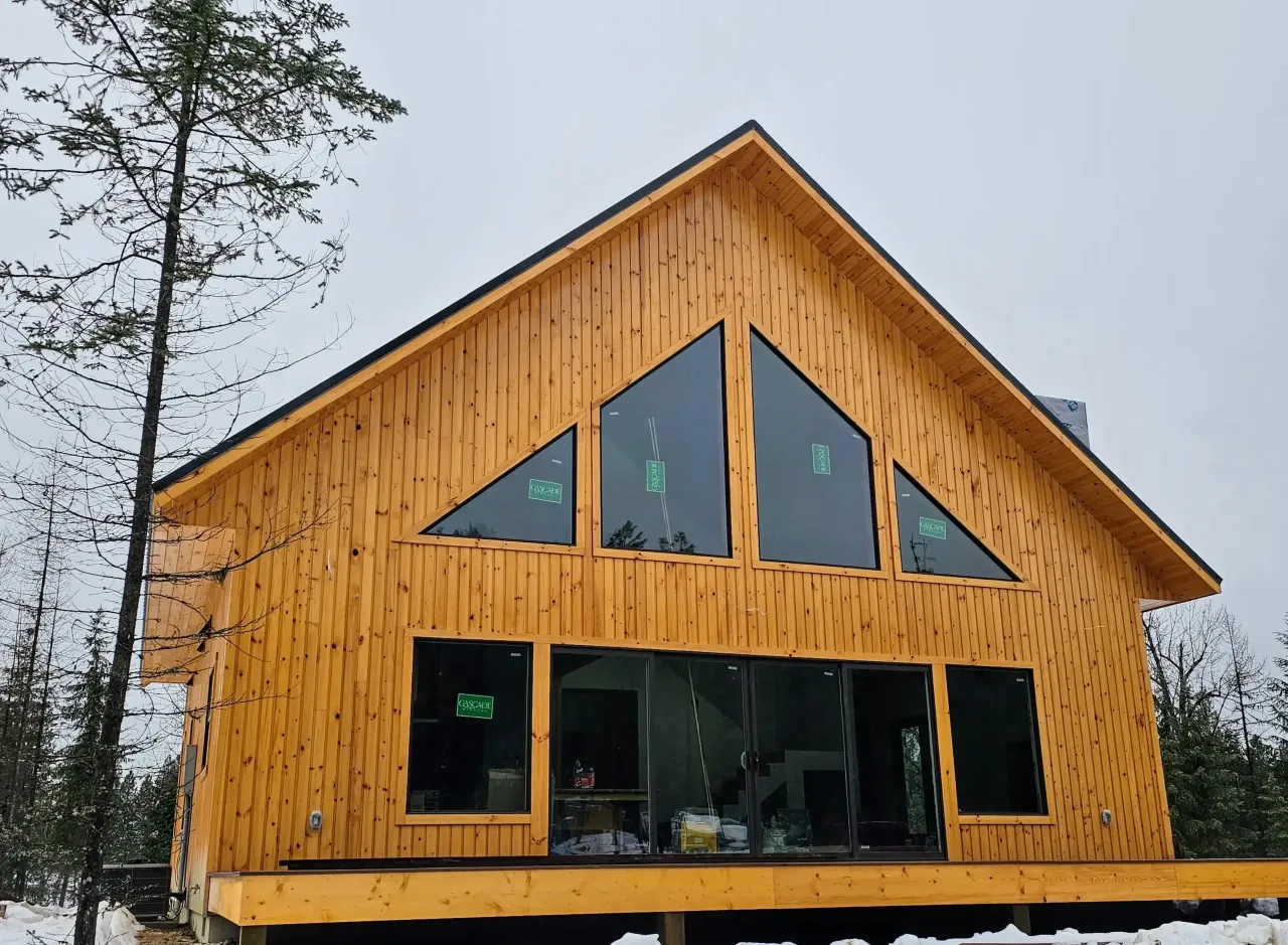 A large wooden house with a lot of windows is surrounded by snow.